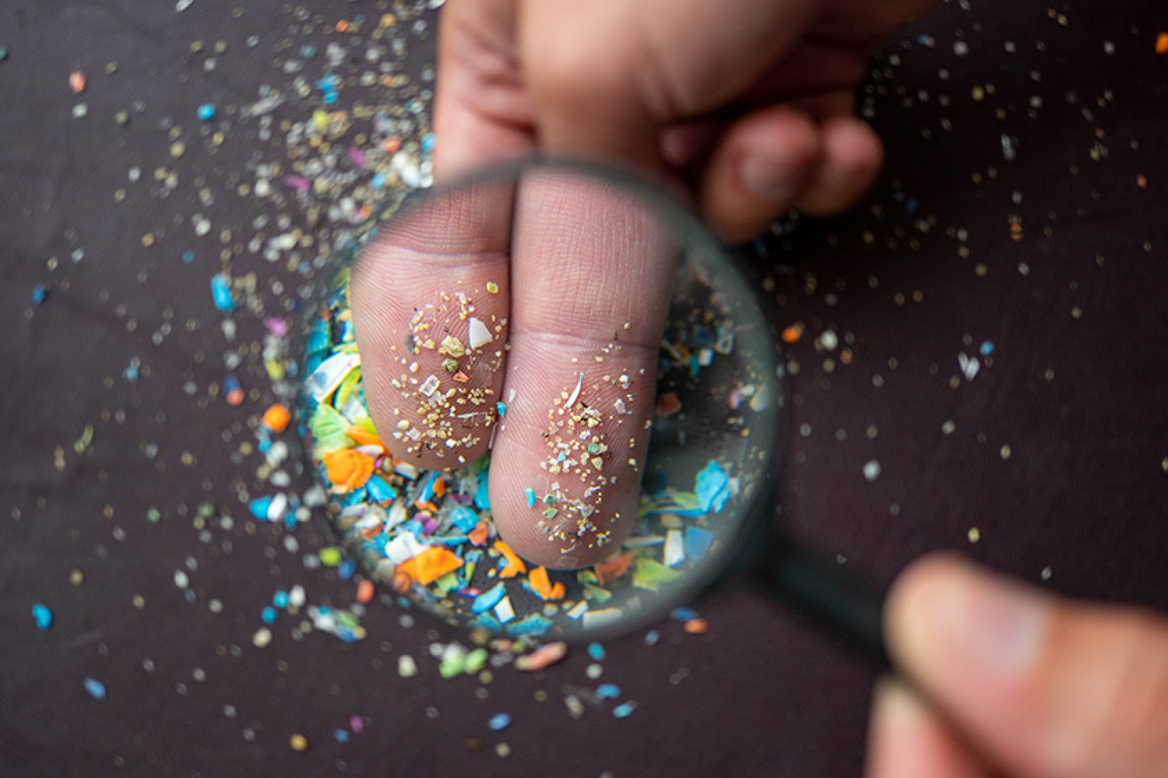 Close-up of micro plastic particles on the fingers under a magnifying glass. Concept for water pollution and global warming. Macro shot on a bunch of microplastics that cannot be recycled